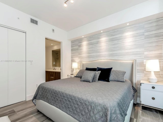 bedroom with tile walls, light hardwood / wood-style flooring, ensuite bathroom, and a closet