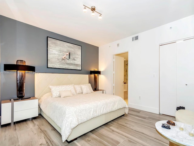 bedroom with light wood-type flooring, ensuite bath, and a closet