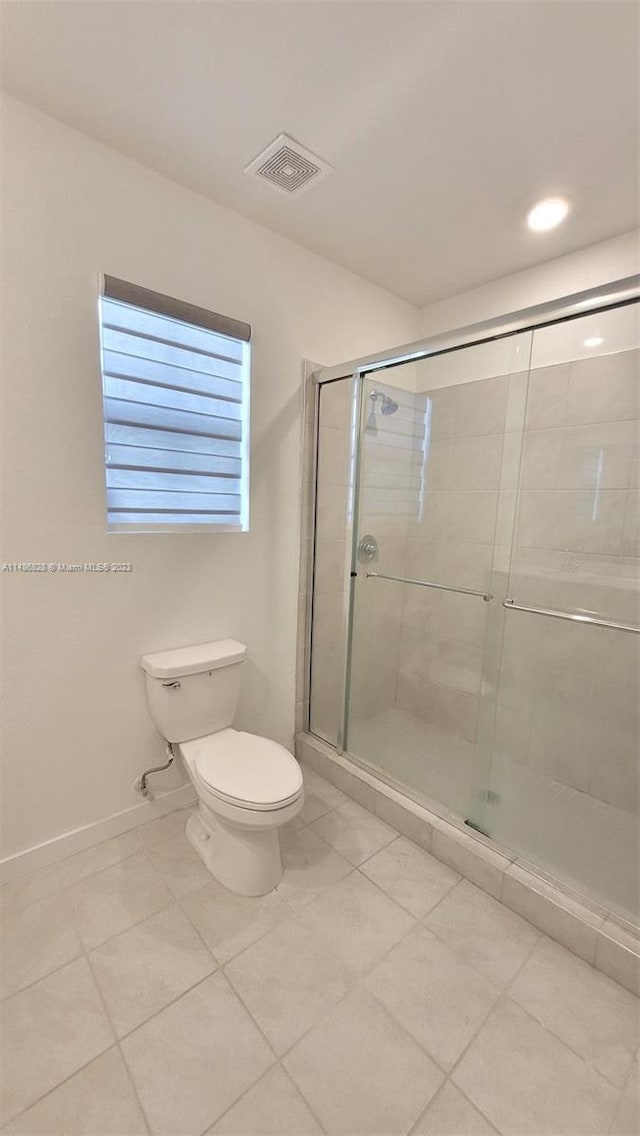 bathroom featuring toilet, tile floors, and a shower with shower door