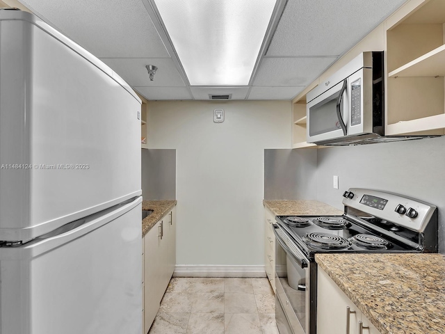 kitchen featuring light stone counters, white cabinetry, appliances with stainless steel finishes, and a drop ceiling