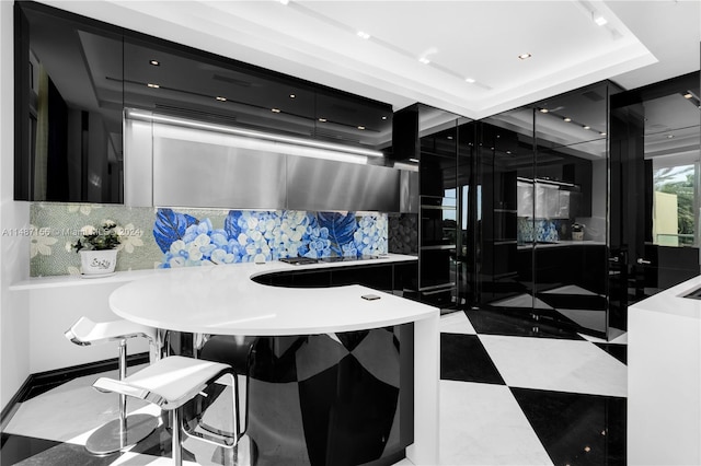 kitchen with tile flooring, a tray ceiling, tasteful backsplash, and a kitchen breakfast bar