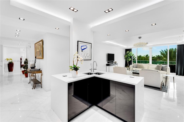 kitchen with a tray ceiling, a kitchen island with sink, an inviting chandelier, sink, and light tile floors