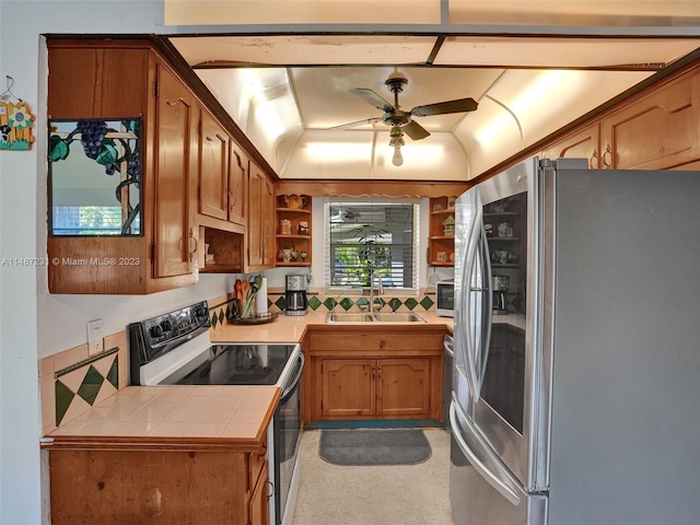 kitchen featuring a tray ceiling, ceiling fan, sink, range with electric stovetop, and stainless steel refrigerator