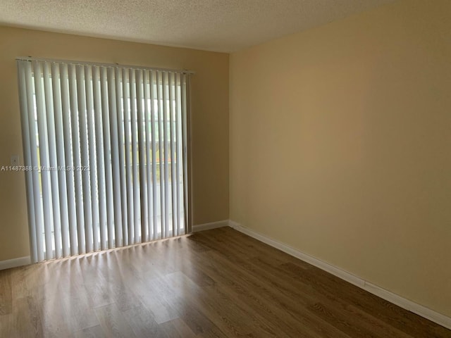 empty room with plenty of natural light, dark hardwood / wood-style flooring, and a textured ceiling