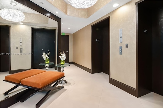 hall featuring a chandelier, a raised ceiling, light tile floors, and elevator