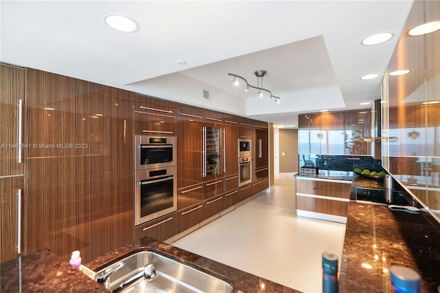 kitchen with light tile floors, dark stone countertops, double oven, black electric cooktop, and track lighting