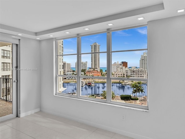 tiled empty room featuring a wealth of natural light, a raised ceiling, and a water view