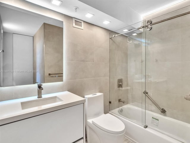 full bathroom featuring combined bath / shower with glass door, tile walls, vanity, and toilet