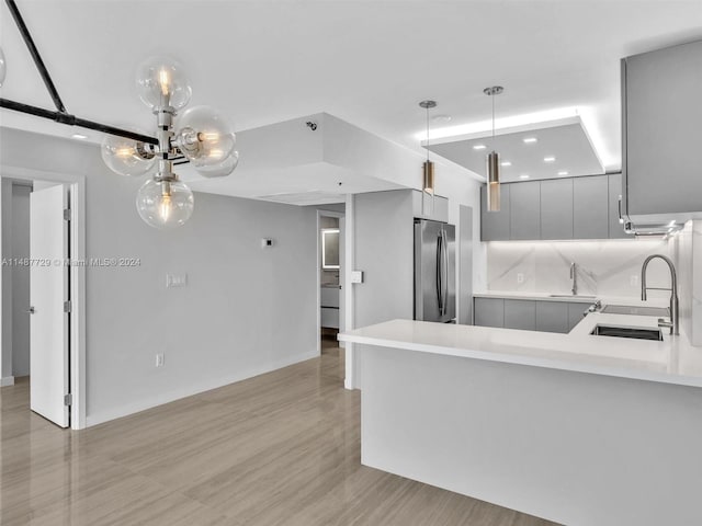 kitchen featuring decorative light fixtures, stainless steel refrigerator, light hardwood / wood-style flooring, gray cabinets, and sink