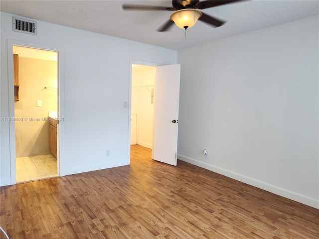 unfurnished bedroom featuring ensuite bath, ceiling fan, wood-type flooring, a spacious closet, and a closet