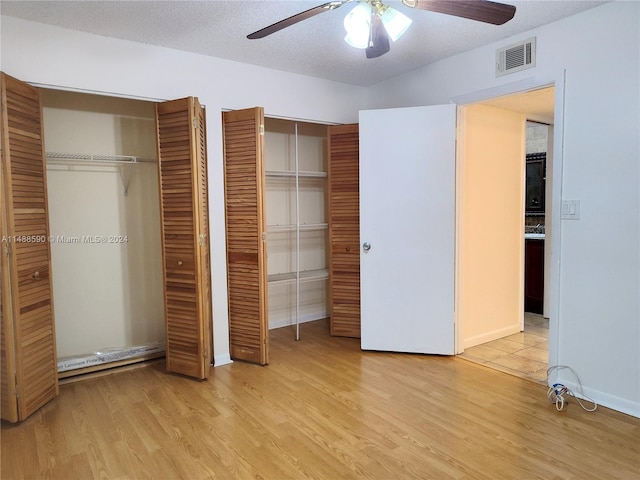 unfurnished bedroom with ceiling fan, light wood-type flooring, a textured ceiling, and two closets