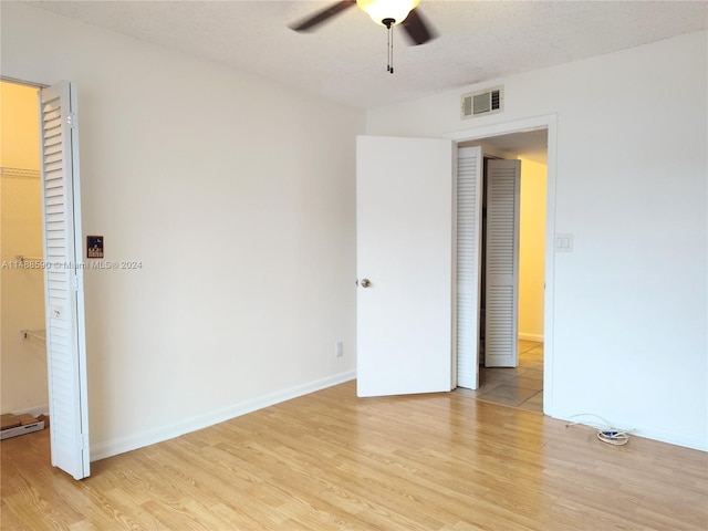 unfurnished bedroom featuring ceiling fan, a textured ceiling, a walk in closet, a closet, and light wood-type flooring