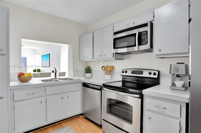 kitchen with white cabinets, appliances with stainless steel finishes, sink, and light wood-type flooring