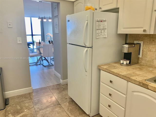 kitchen with white refrigerator, tasteful backsplash, light tile flooring, and white cabinets