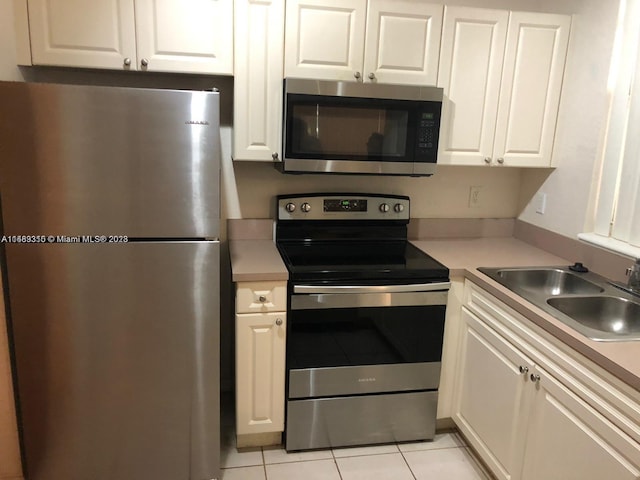 kitchen featuring stainless steel appliances, light tile floors, white cabinetry, and sink