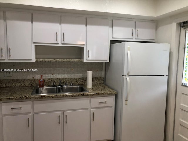 kitchen featuring dark stone counters, white cabinetry, backsplash, and white fridge