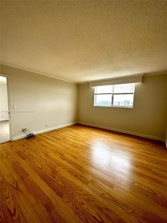 empty room with light wood-type flooring, ornamental molding, and a textured ceiling