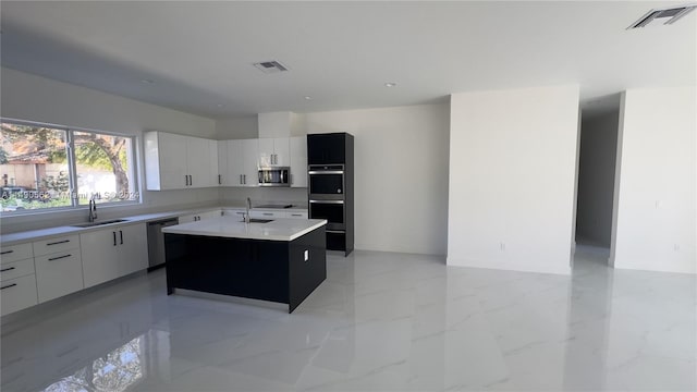 kitchen with light tile floors, a center island with sink, appliances with stainless steel finishes, white cabinets, and sink