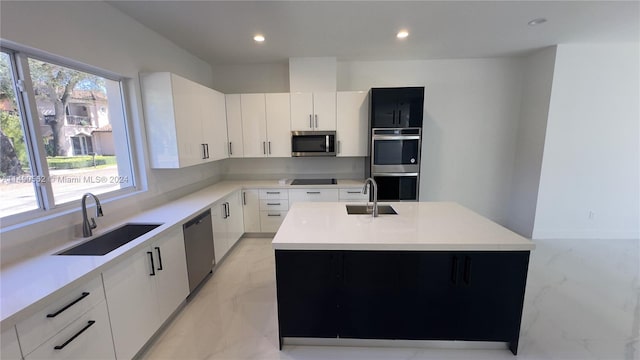 kitchen featuring sink, white cabinets, appliances with stainless steel finishes, a center island with sink, and light tile flooring