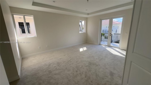 unfurnished room with a raised ceiling, light carpet, and french doors