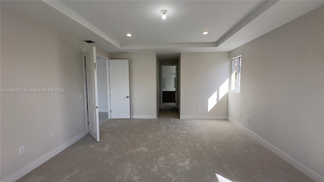 unfurnished bedroom with light carpet and a raised ceiling