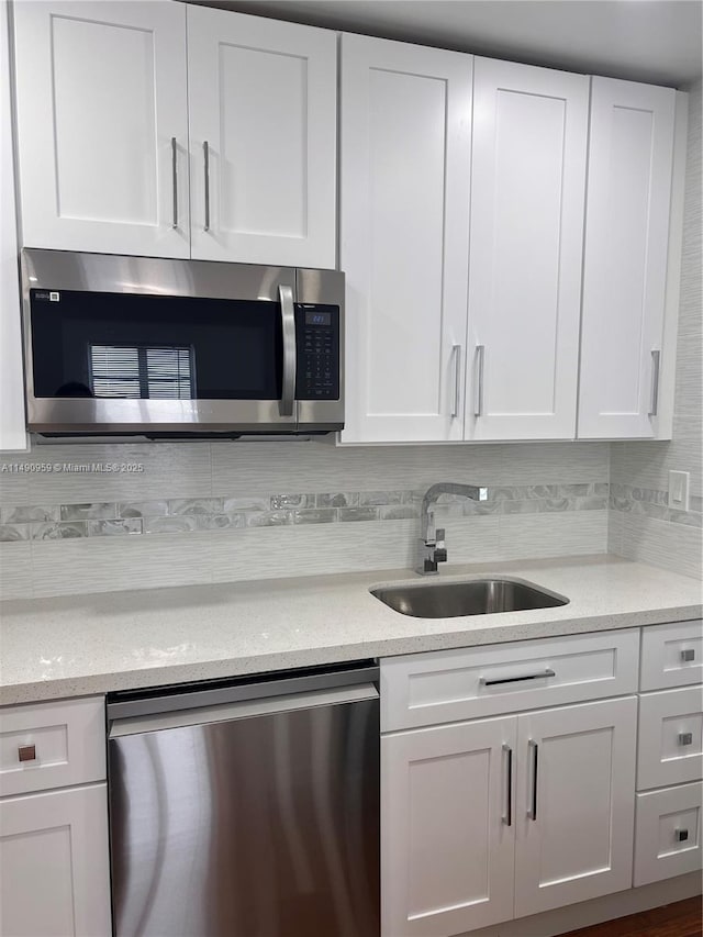 kitchen featuring light stone counters, decorative backsplash, appliances with stainless steel finishes, white cabinetry, and a sink