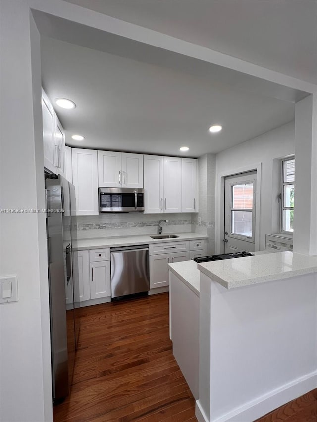 kitchen with appliances with stainless steel finishes, white cabinets, a sink, light stone countertops, and a peninsula