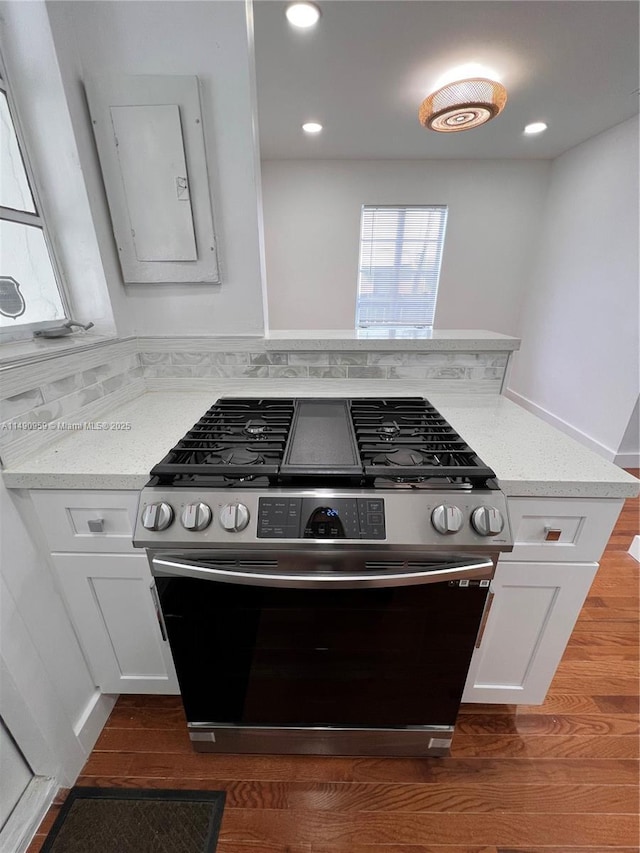 kitchen with light stone countertops, dark wood-style flooring, white cabinetry, stainless steel gas range, and decorative backsplash