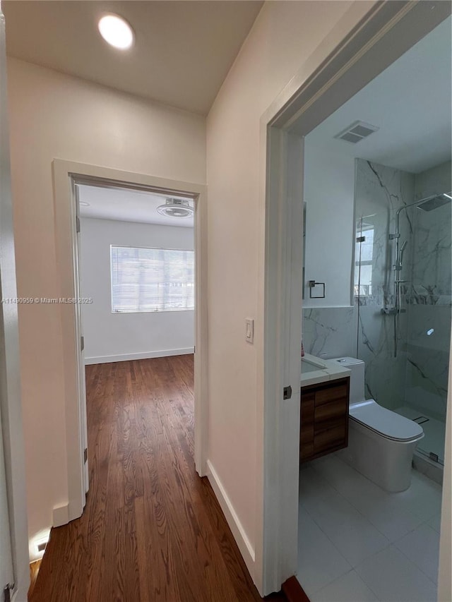 corridor featuring dark wood-style flooring, visible vents, and baseboards