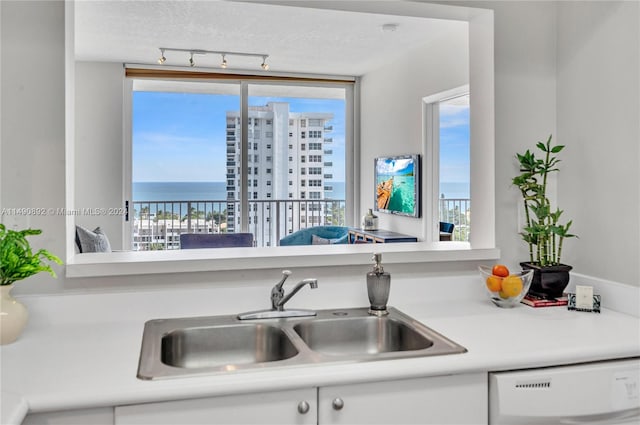 kitchen with dishwashing machine, a textured ceiling, sink, and a water view