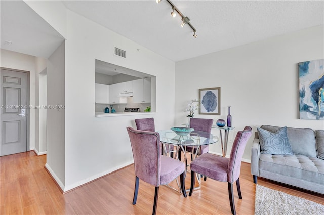 dining space featuring track lighting, a textured ceiling, and light hardwood / wood-style flooring