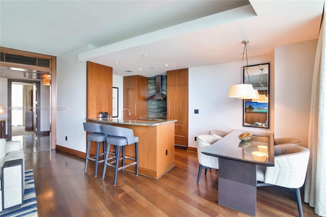 kitchen featuring wall chimney range hood, a kitchen breakfast bar, dark hardwood / wood-style flooring, and decorative light fixtures