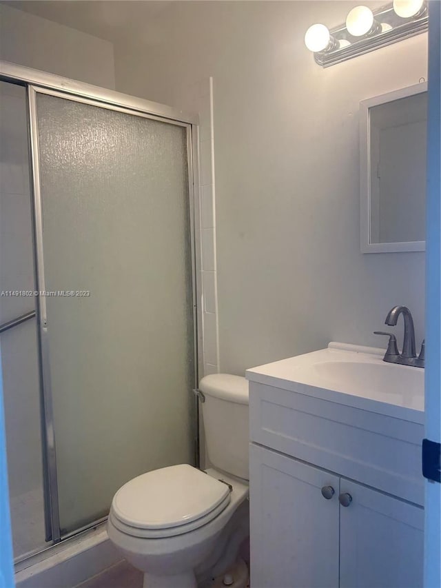 bathroom featuring toilet, vanity, and a shower with shower door