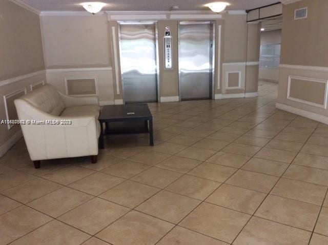 unfurnished living room with elevator, light tile flooring, and ornamental molding