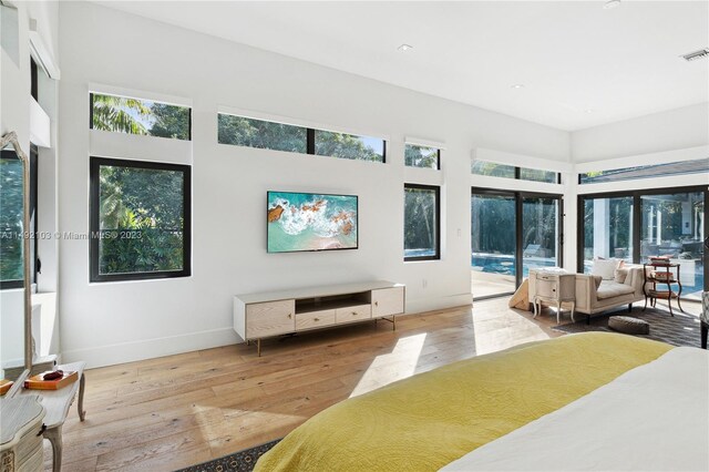 bedroom with access to outside, multiple windows, a towering ceiling, and light hardwood / wood-style flooring