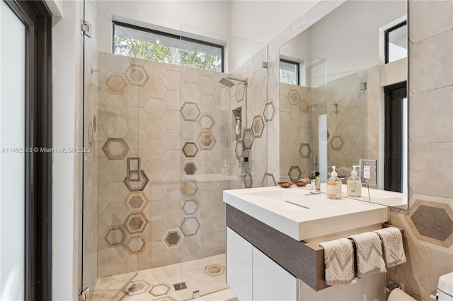 bathroom featuring tile walls, toilet, vanity, and a shower with shower door