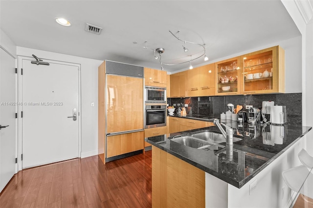 kitchen with kitchen peninsula, built in appliances, sink, dark wood-type flooring, and a kitchen breakfast bar