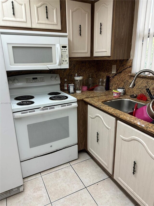 kitchen with sink, tasteful backsplash, dark stone counters, white appliances, and light tile patterned flooring