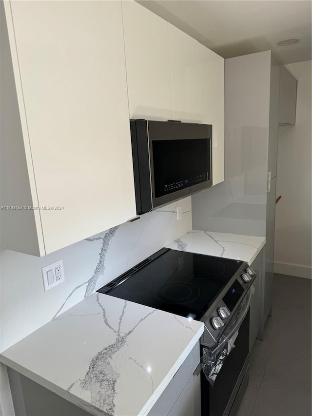 kitchen featuring tasteful backsplash, black range with electric stovetop, white cabinets, and light stone countertops