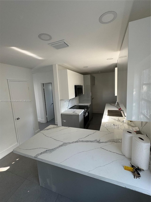 kitchen featuring light stone countertops, black appliances, white cabinetry, dark tile floors, and sink