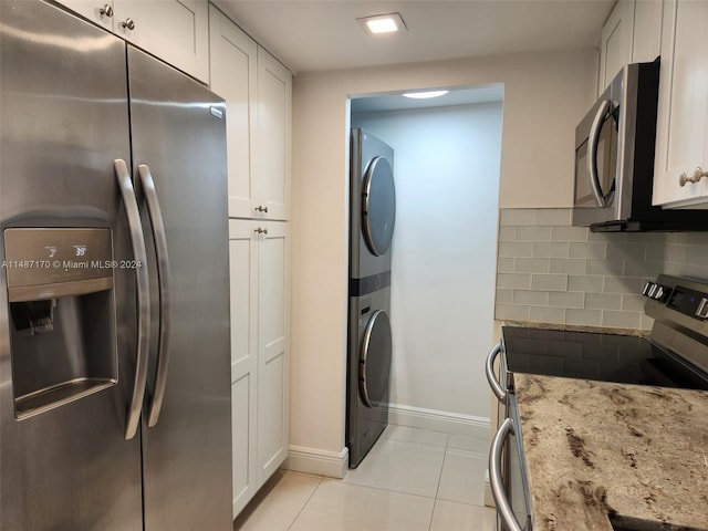 kitchen featuring stacked washing maching and dryer, white cabinetry, light stone counters, and stainless steel appliances