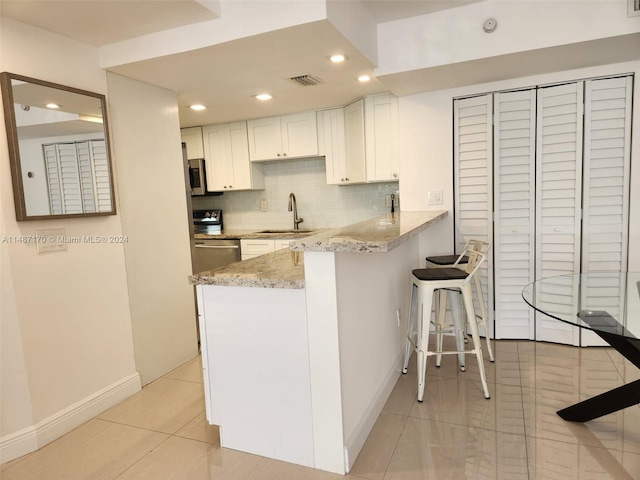 kitchen with light tile floors, tasteful backsplash, white cabinets, light stone counters, and sink