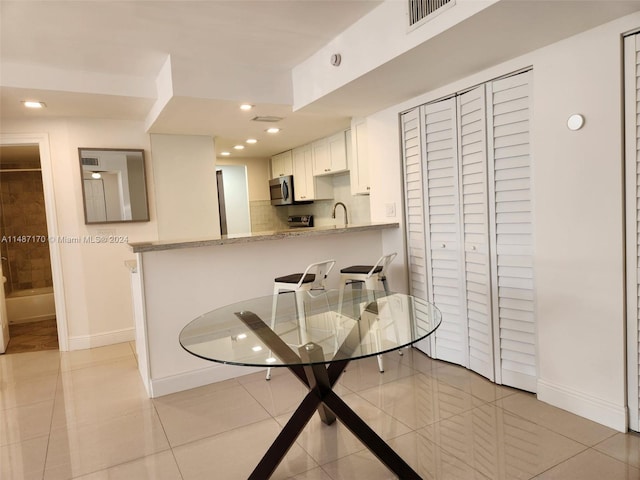 kitchen with kitchen peninsula, light stone countertops, a kitchen breakfast bar, light tile floors, and white cabinets