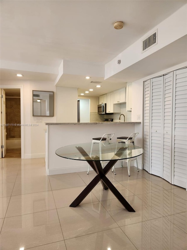 kitchen with light stone countertops, kitchen peninsula, sink, light tile floors, and white cabinets