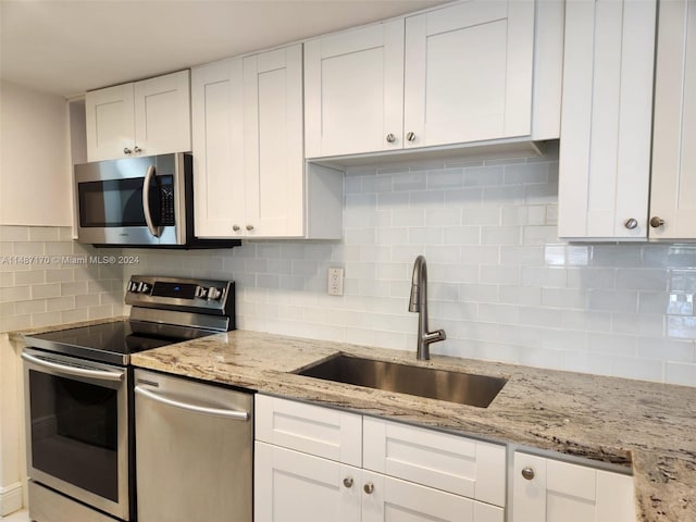 kitchen featuring sink, white cabinets, stainless steel appliances, light stone countertops, and tasteful backsplash