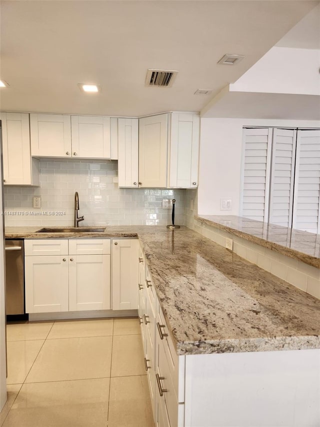 kitchen featuring sink, light stone counters, white cabinets, stainless steel dishwasher, and tasteful backsplash