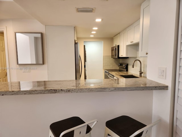 kitchen with kitchen peninsula, light stone countertops, backsplash, appliances with stainless steel finishes, and white cabinets