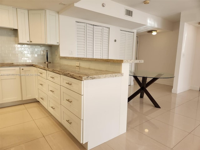 kitchen with light tile floors, light stone countertops, tasteful backsplash, and white cabinets