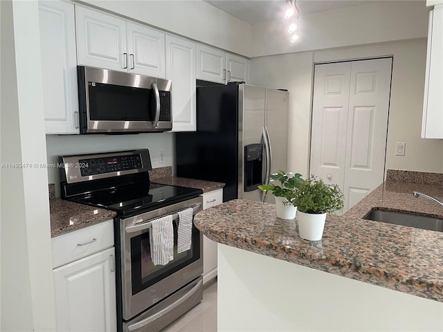 kitchen featuring appliances with stainless steel finishes, white cabinetry, dark stone counters, and sink