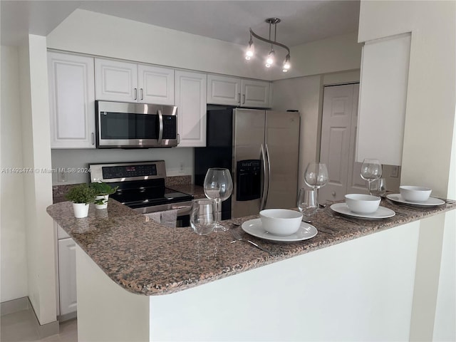 kitchen featuring kitchen peninsula, stainless steel appliances, white cabinets, and dark stone counters